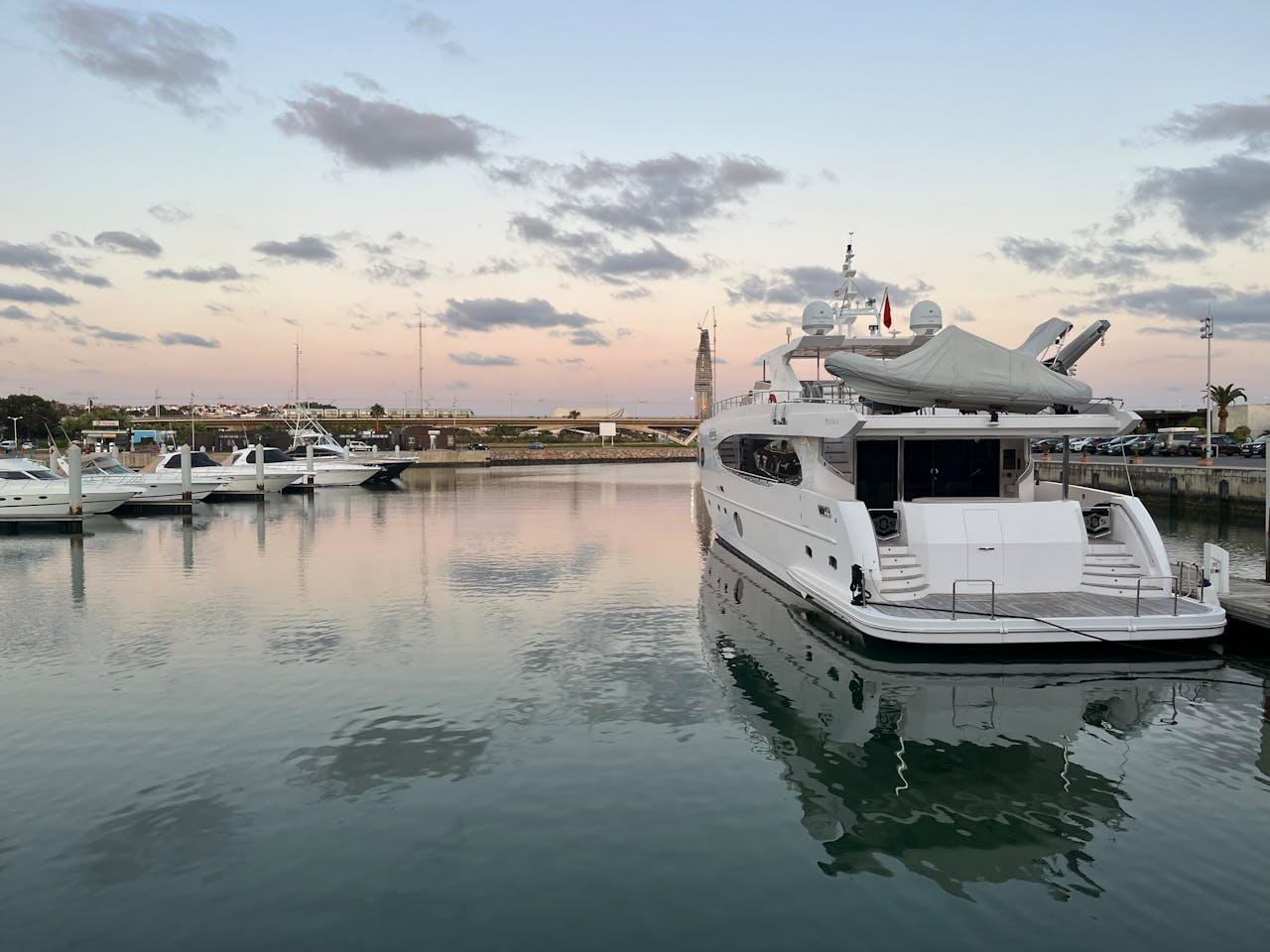 A luxurious motor yacht docked in Rabat marina at sunset surrounded by calm waters and sky reflections.