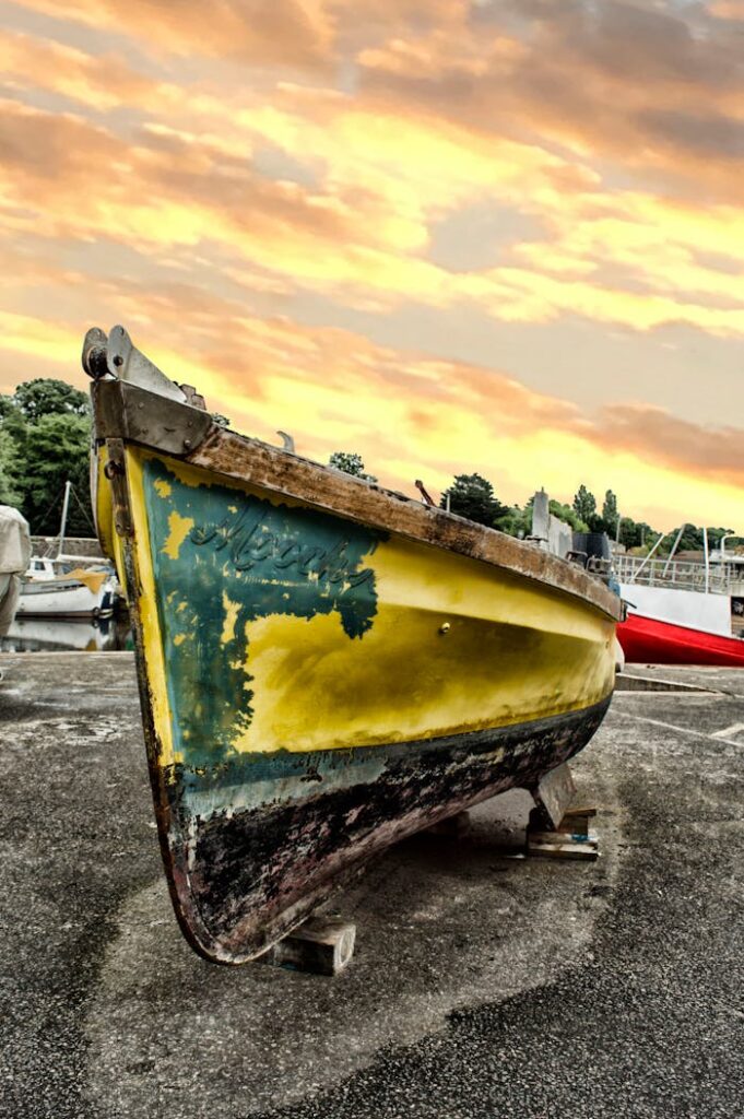 A weathered yellow boat in a dry dock during a vibrant sunset in Devon, UK, with scenic clouds overhead.